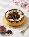 Chocolate and cream tart on a gold plate, styled on a white marble surface with pink blossoms, a small bowl of chocolate sauce, chocolate chunks, and a gold fork.