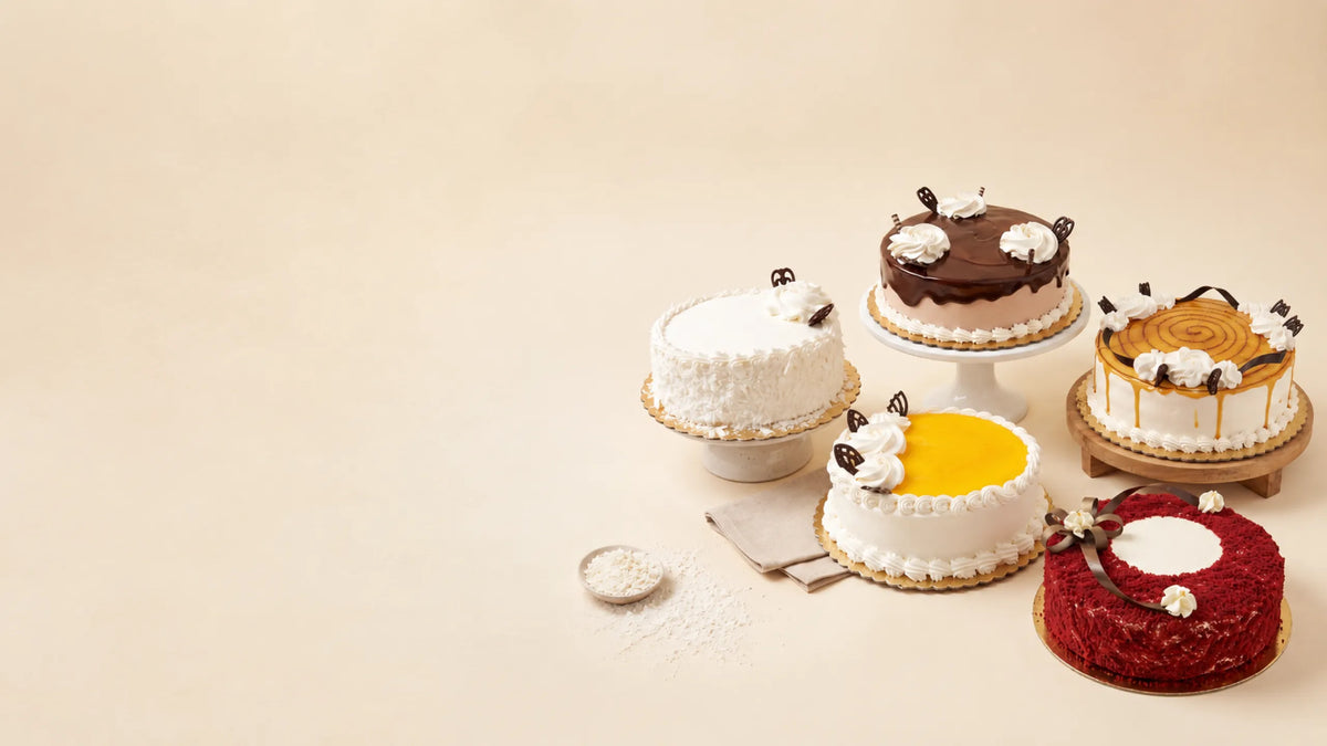 Five decorated cakes in assorted flavors and colors, including chocolate, vanilla, red velvet, and caramel-topped designs, arranged on stands against a warm beige background.